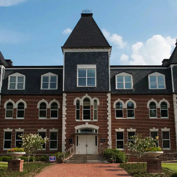 A large, three-story brick Schools building with a slate roof and tower features arched windows and a central entrance amid landscaped grounds under partly cloudy skies. Inside, Power HVAC Services Commercial Air Duct Cleaning of schools ensures pristine air ducts for all inhabitants in the GTA area.