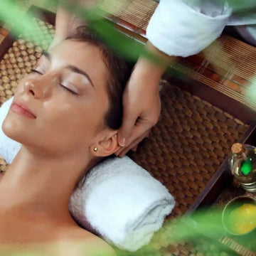 Amidst the tranquility of a bamboo mat and green leaves, a person enjoys a head massage on a soft towel. Nearby essentials like a small bottle create a serene oasis reminiscent of the calm one seeks after efficient Commercial Air Duct Cleaning by Power HVAC Services in the busy GTA area.