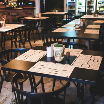 A restaurants interior features black tables and chairs with menus and small plant centerpieces. Background shelves of bottles reveal a meticulously clean space, potentially thanks to Power HVAC Services Commercial Air Duct Cleaning of restaurants and kitchen hood cleaning.