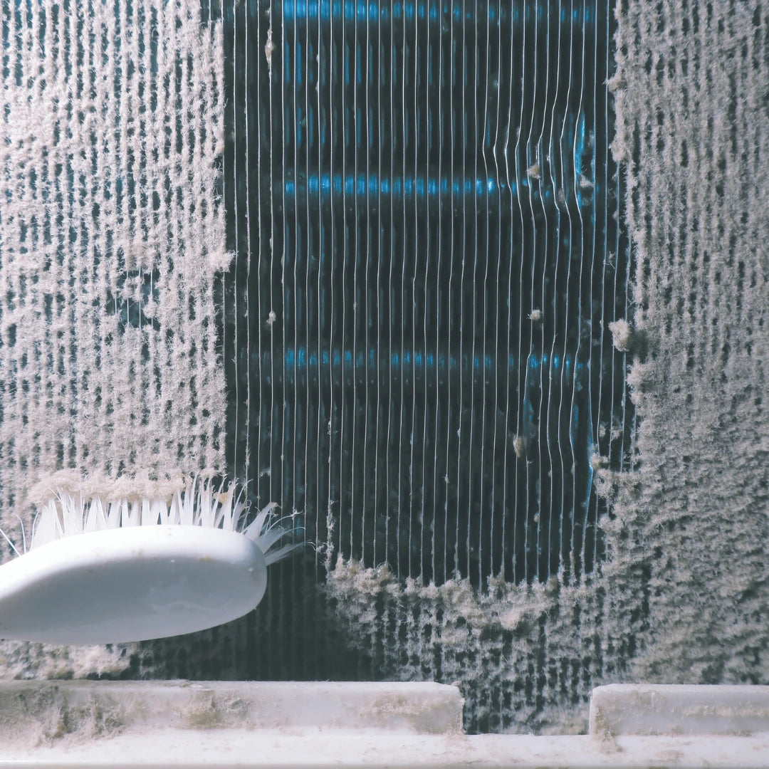 A close-up shows dust being cleaned from an air conditioner coil with a white brush, revealing the blue metal beneath. This step in Power HVAC Services Commercial Fan Coil Cleaning enhances indoor air quality, ensuring a healthier breathing environment.