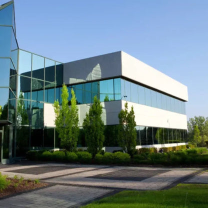 A modern office building with large glass windows is surrounded by trees and a paved walkway on a sunny day, using Power HVAC Services Commercial Air Duct Cleaning to maintain its sleek appearance.