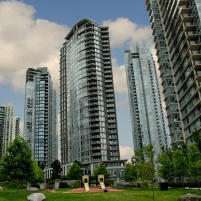 Tall glass skyscrapers with curved facades overlook greenery and a playground under partly cloudy skies, reminding city dwellers that Power HVAC Services Air Duct Cleaning of Condos is essential for maintaining clean, fresh air.