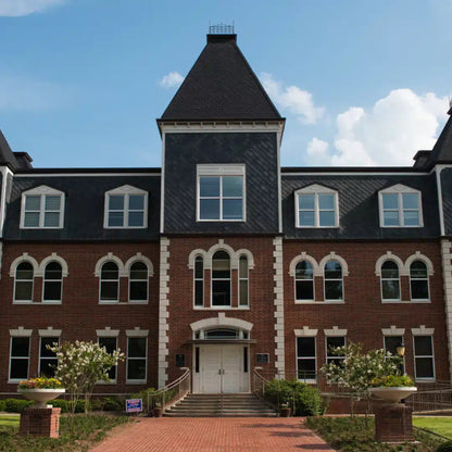 A large, three-story brick Schools building with a slate roof and tower features arched windows and a central entrance amid landscaped grounds under partly cloudy skies. Inside, Power HVAC Services Commercial Air Duct Cleaning of schools ensures pristine air ducts for all inhabitants in the GTA area.