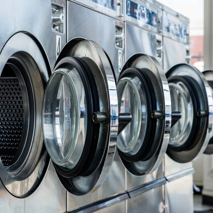 In a laundromat, open industrial front-loading washing machines highlight the need for regular maintenance. Power HVAC Services offers Laundromat Dryer Duct Cleaning to ensure optimal performance.